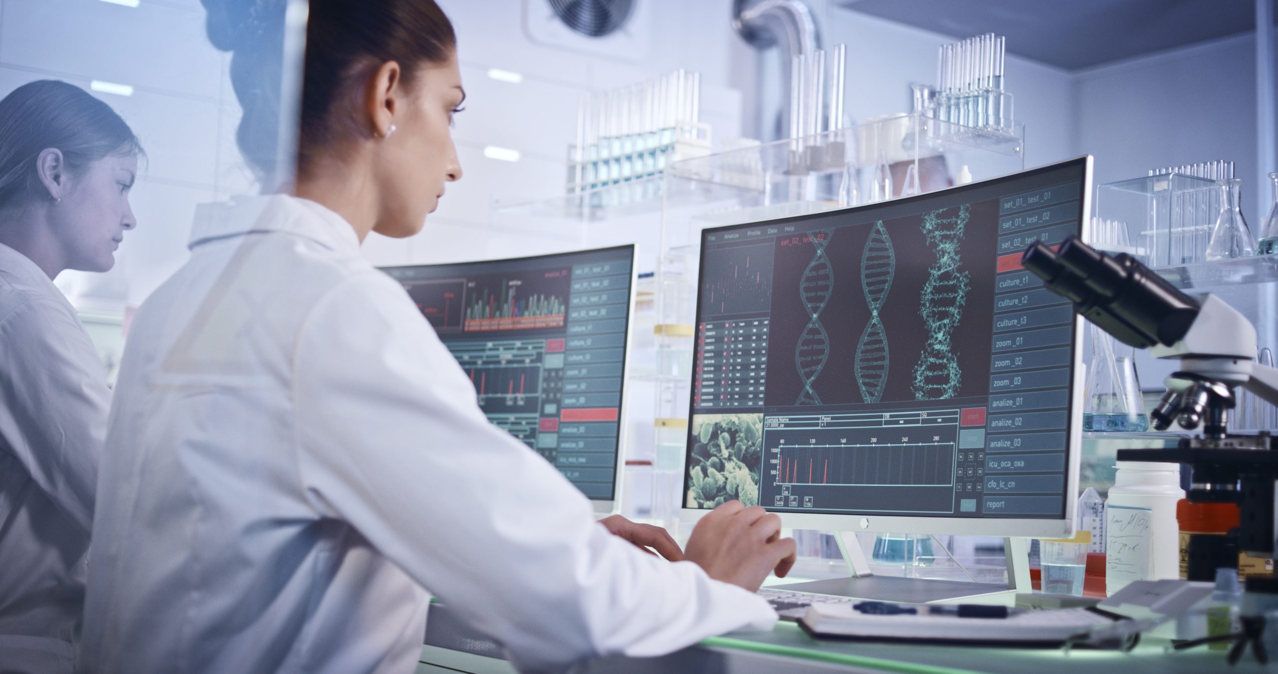 Female research team studying DNA mutations. Computer screens with DNA helix in foreground